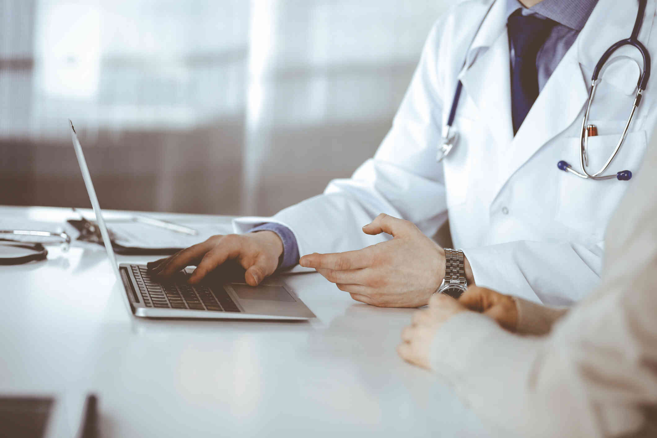 A close up of a doctor sitting at a table with his patient and showing her some information on a computer.